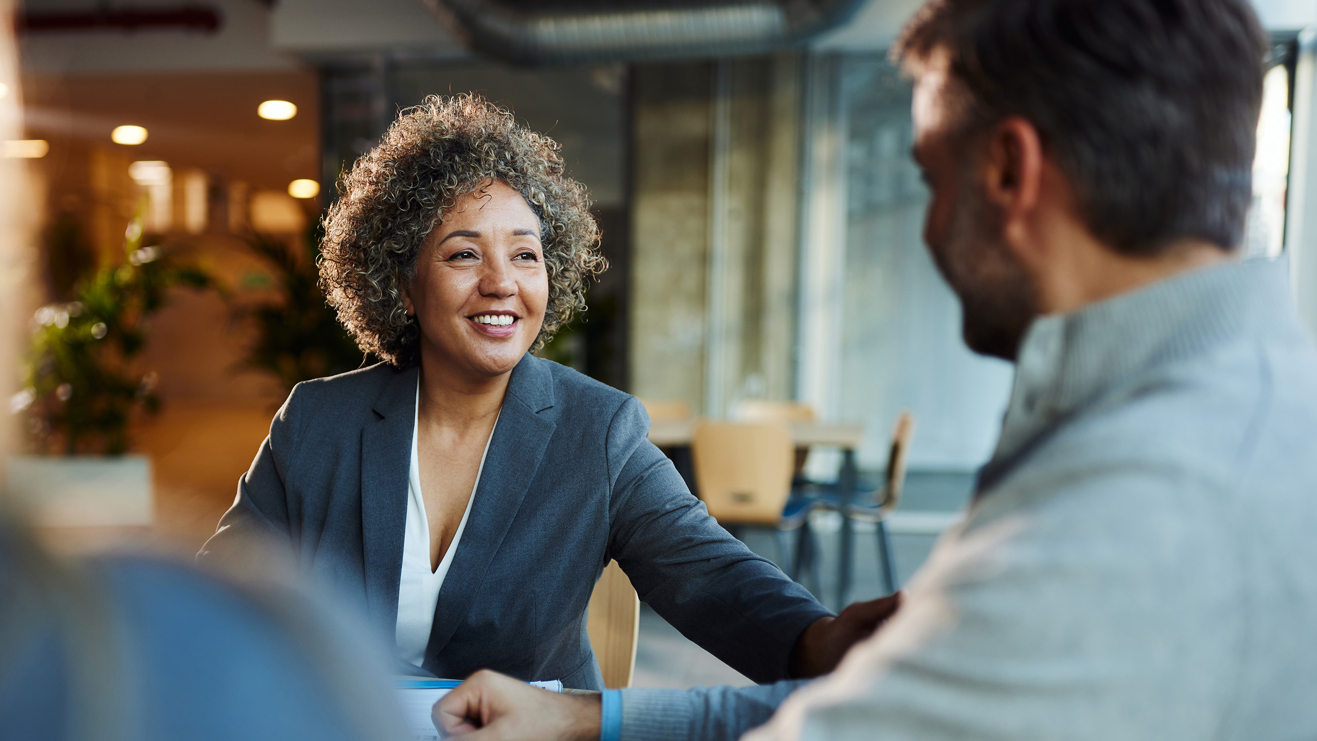 Groupe de personnes assises autour d’une table dans un espace de bureau moderne et ouvert, en pleine conversation.